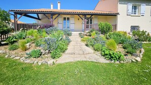 A house with a tiled roof, a covered porch, and a garden with various plants and flowers. - Villa de Charme Avec Piscine - Idéale Pour des Vacances en Famille ou Entre Amis (Julienne)