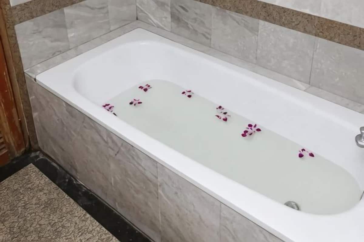 A white bathtub with rose petals in a bathroom with marble walls and a black floor.