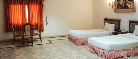 A hotel room with two beds, a chair, a painting on the wall, and a window with curtains.