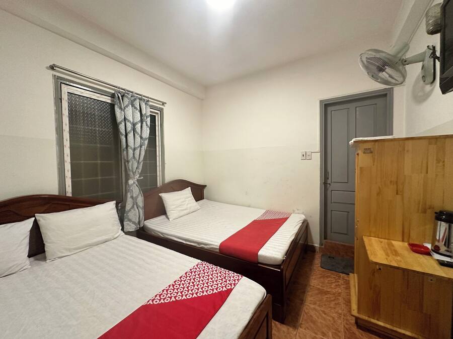 A bedroom with two beds, a window with curtains, a wooden wardrobe, and a wall-mounted fan.