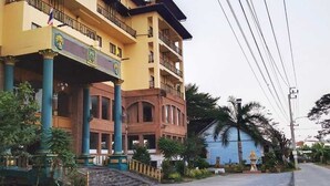 A multi-story hotel with a yellow facade, balconies, and a blue building in the background. - OYO 75466 13 Coins Bang Yai Hotel (Bang Yai)