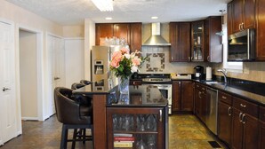 A modern kitchen with dark wooden cabinets, a central island with bar stools, a stainless steel refrigerator, and a built-in oven.
