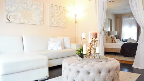 A modern living room with a white sofa, a tufted ottoman, and a decorative table with candles.