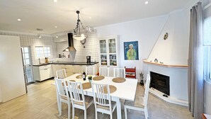 A modern kitchen with white cabinetry, a central island, and a dining area with white chairs and a white table.