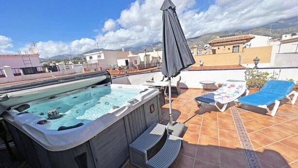 A rooftop terrace with a hot tub, lounge chairs, and a view of the surrounding landscape.