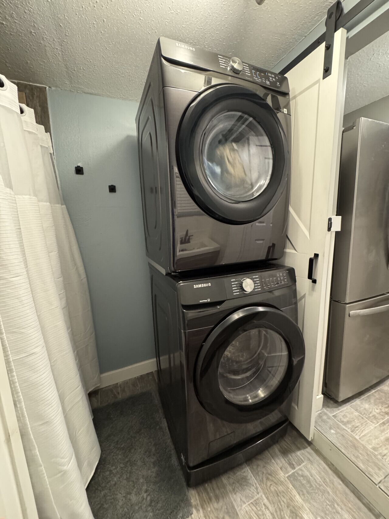 Een kleine wasruimte met een Samsung wasmachine en droger die boven elkaar geplaatst zijn.