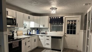 Une cuisine de taille réduite, avec des meubles blancs, un four à micro-ondes, une cuisinière et un lave-vaisselle.