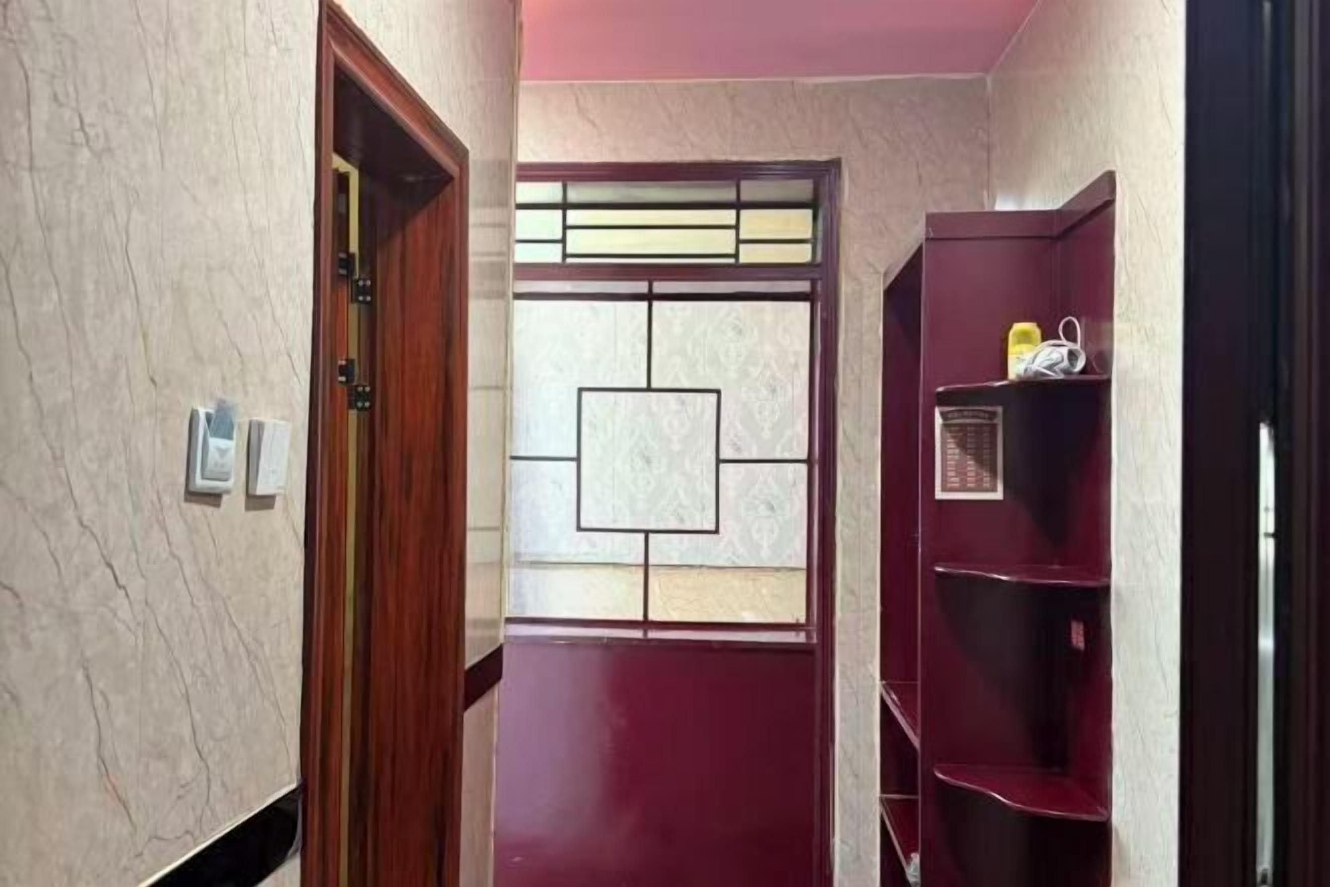 A hallway with a door, a wall-mounted shelf with items, and a decorative window.