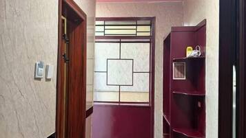 A hallway with a door, a wall-mounted shelf with items, and a decorative window.