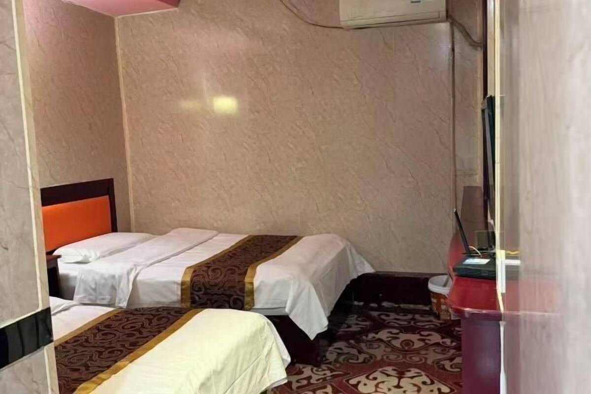 Quarto de hotel pequeno com duas camas, uma lixeira vermelha e um ar condicionado fixado na parede.