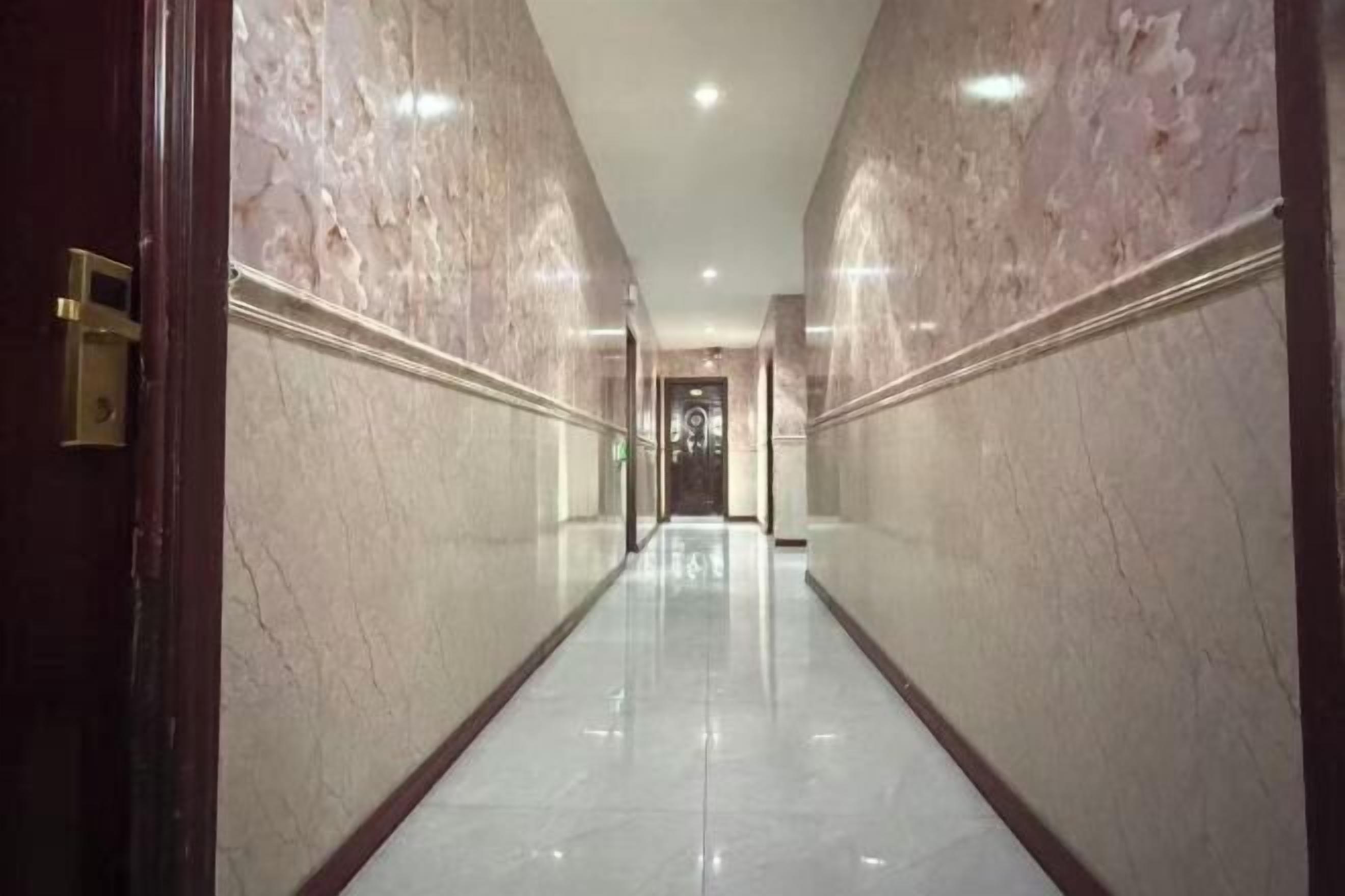 A long, narrow hallway with marble walls and a polished floor, leading to a door at the end.