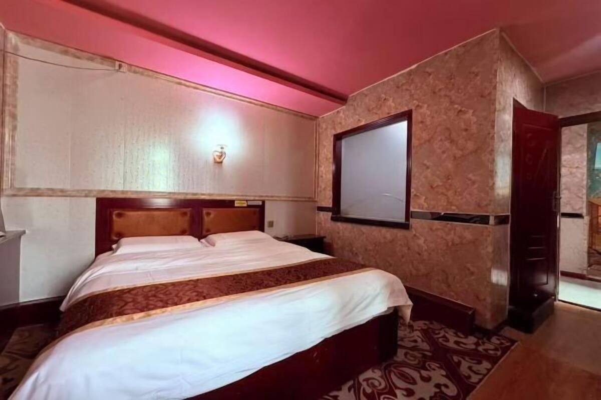 Quarto de hotel com cama, televisão fixada na parede e porta para outro espaço.
