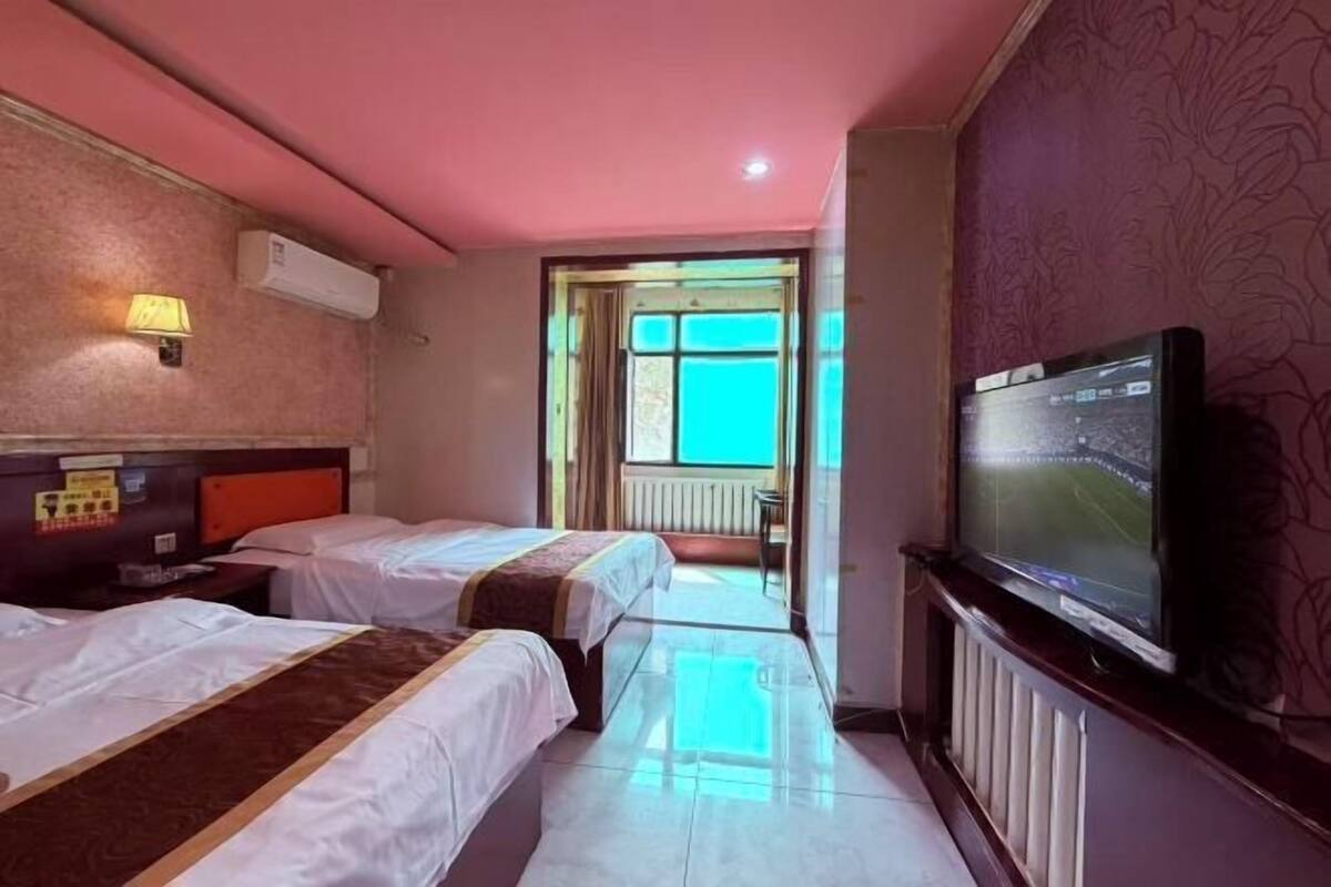 Quarto de hotel com duas camas, televisão e vista para o exterior.