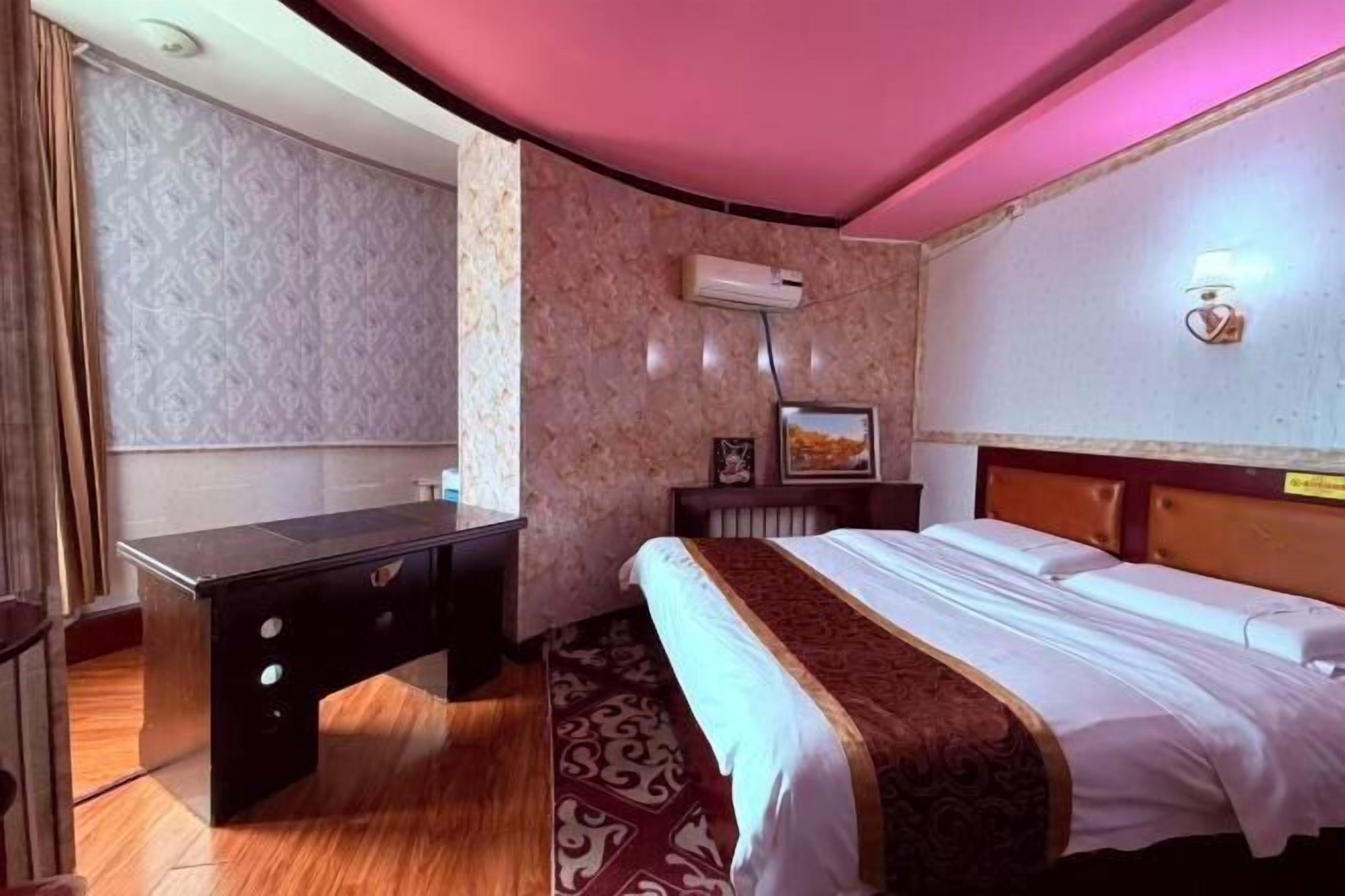 Une chambre d’hôtel comprenant un lit, un bureau, une chaise, un climatiseur fixé au mur et un tapis à motifs.