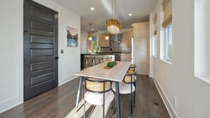 A modern kitchen with a wooden table, bar stools, and a chandelier. - Ultra Heated Rooftop Pool! Arcade, Elevator, EV Charger, Sleeps 12, Full Home (Nashville)