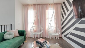 A room with a green sofa, two white hanging chairs, a round coffee table with books and a remote, and a black and white chevron-patterned wall. - Ultra Heated Rooftop Pool! Arcade, Elevator, EV Charger, Sleeps 12, Full Home (Nashville)