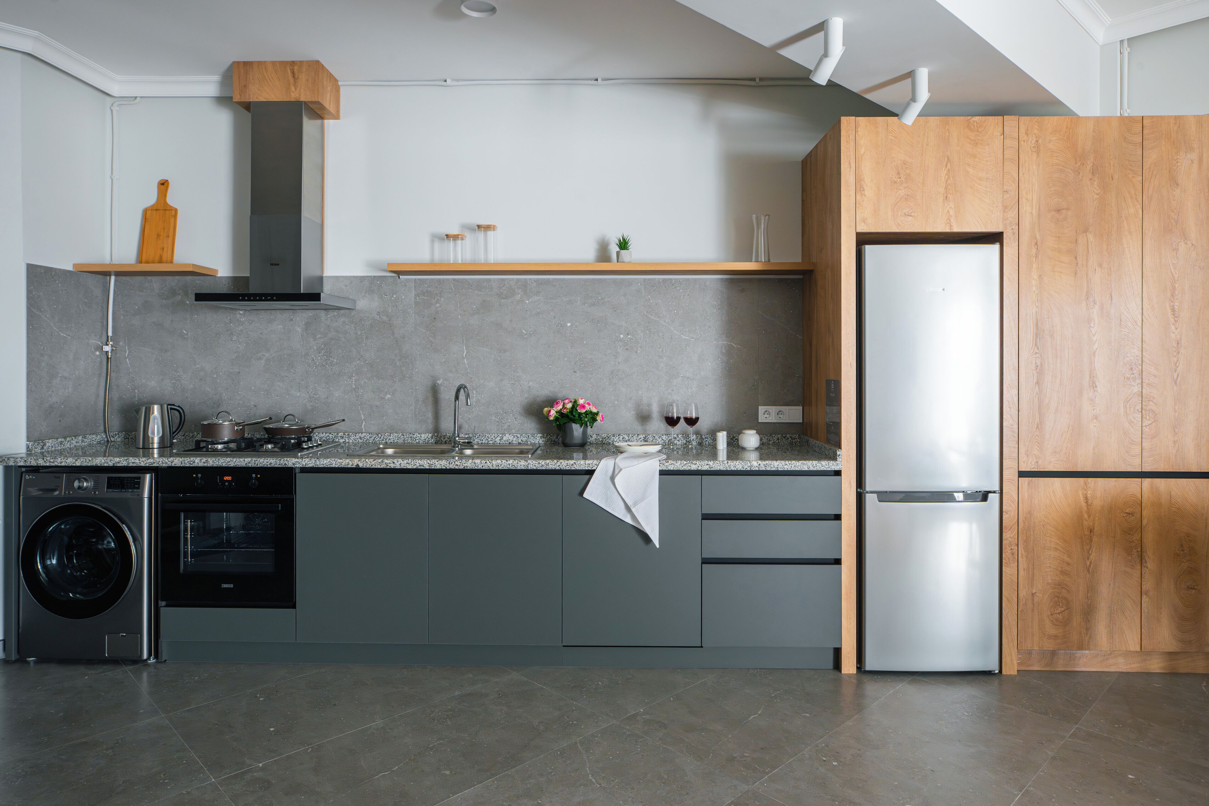 Una cocina moderna con armarios grises, un refrigerador de acero inoxidable, horno empotrado y lavadora.