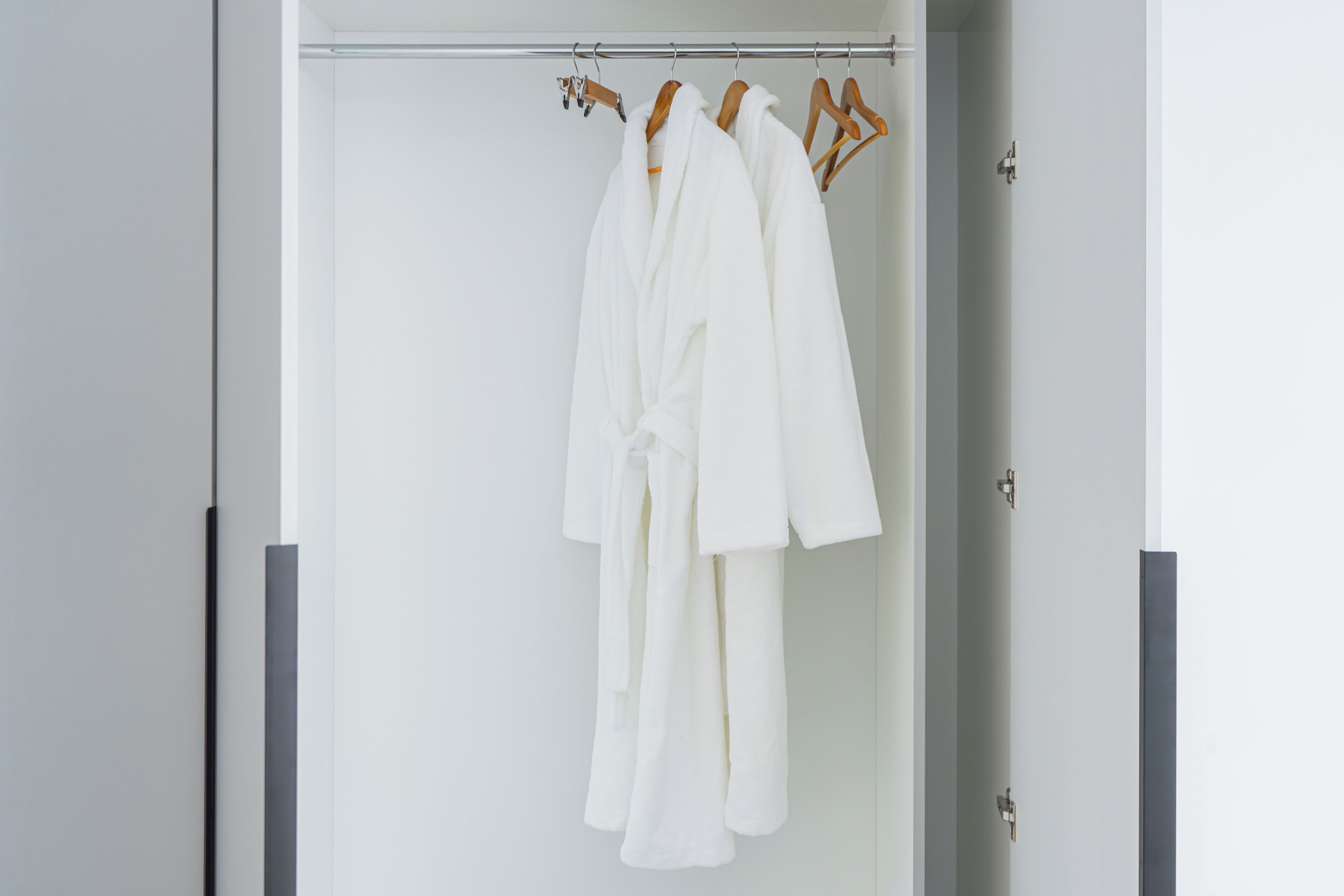 Un vestit blanc penjat en una barra de metall a una habitació amb una porta i un panell vertical negre.