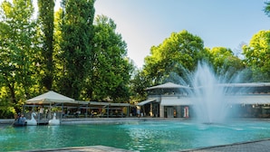 Ein Pool mit einer Fontäne, umgeben von Bäumen und überdachten Sitzbereichen.