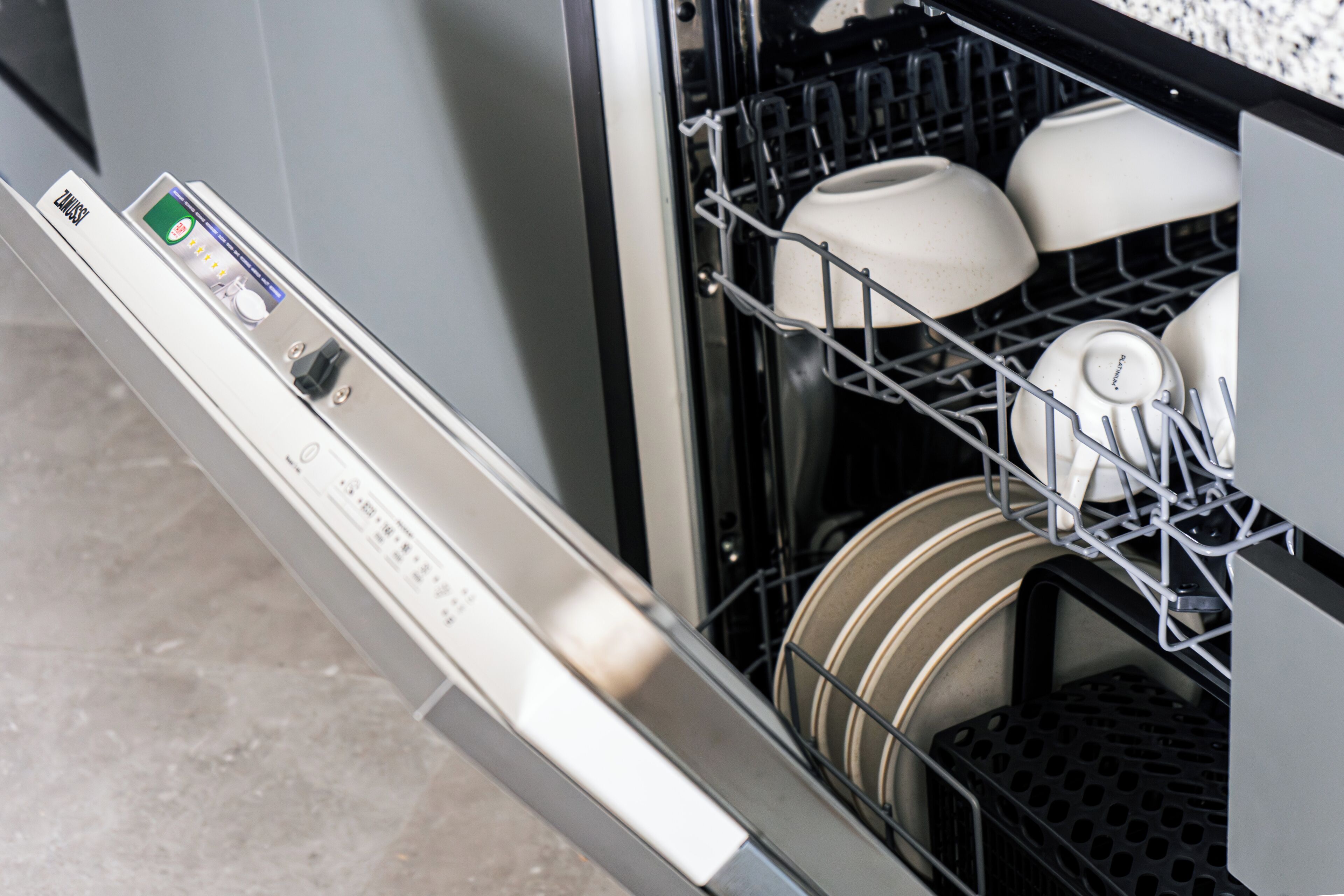 An open dishwasher with white dishes and a control panel.