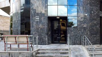 A modern building entrance with a marble facade, a set of stairs leading up to the entrance, and a bench outside.