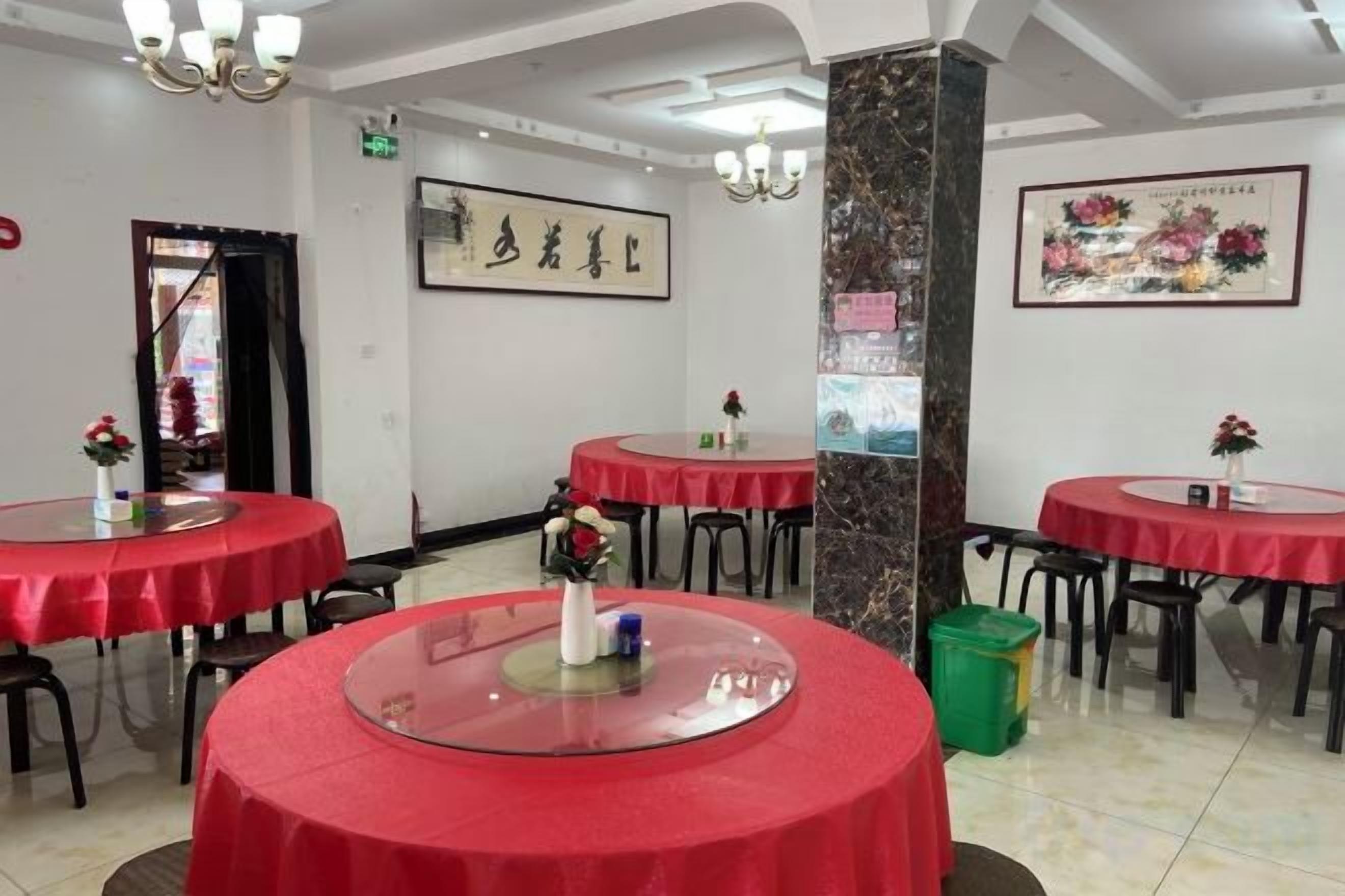 A restaurant interior with round tables, chairs, and red tablecloths.