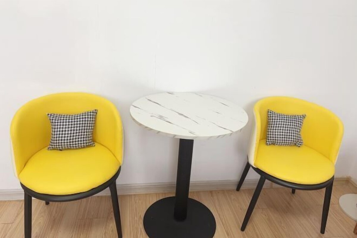 Twee gele stoelen met geruit kussens, een witte ronde tafel en een zwart onderstel.