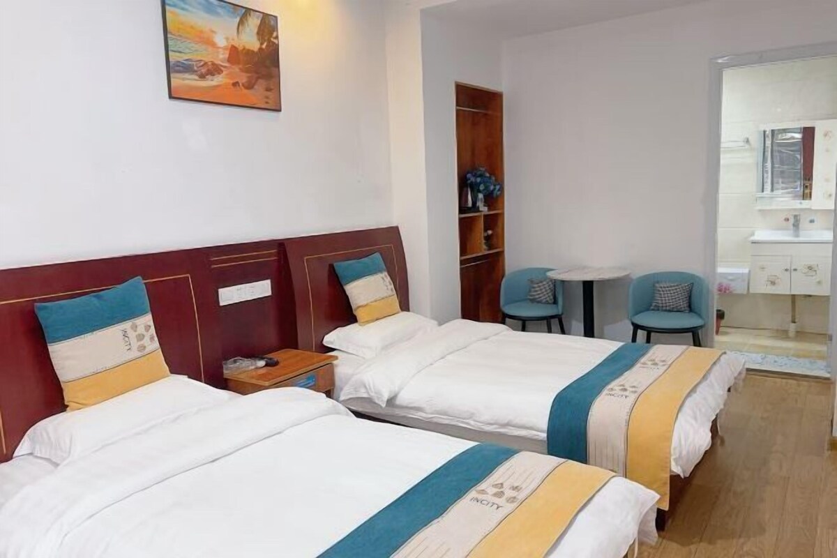 Een hotelkamer met twee bedden, een kleintje tafeltje, een stoel, een boekenkast en een badkamer zichtbaar door een open deur.