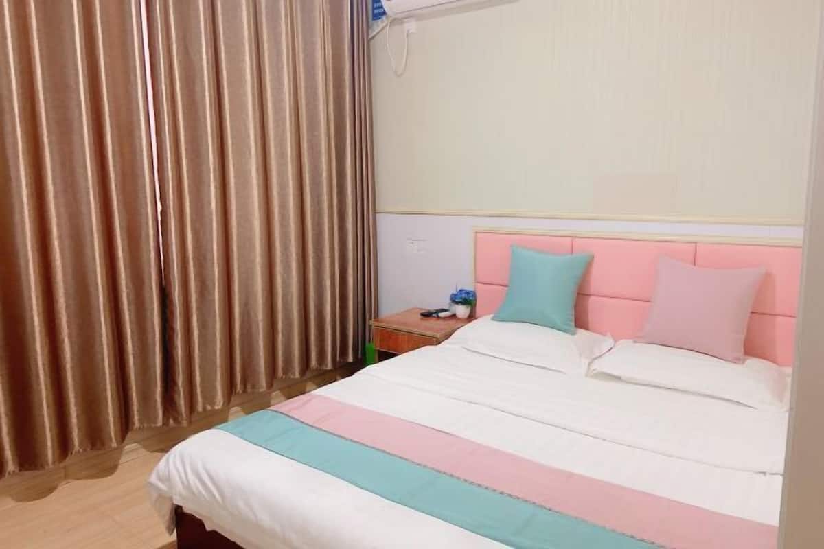 Een hotelkamer met een bed, gordijnen, een nachtkastje en een wandairconditioner.