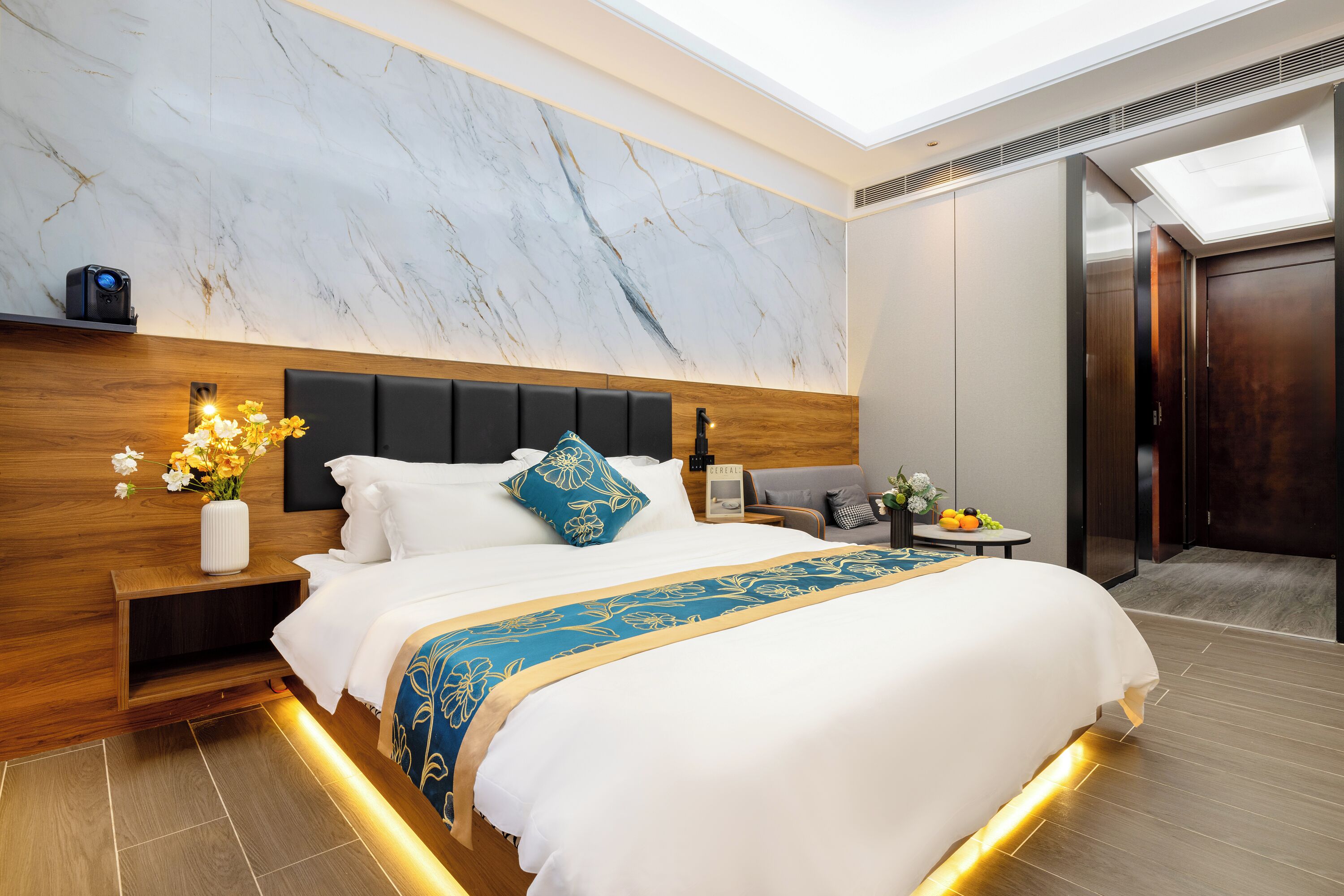 A modern hotel room with a large bed, wooden headboard, marble wall, and a skylight.
