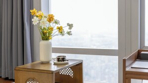 Una mesita auxiliar de madera con un jarrón blanco que contiene flores amarillas y blancas, una taza y un plato encima.