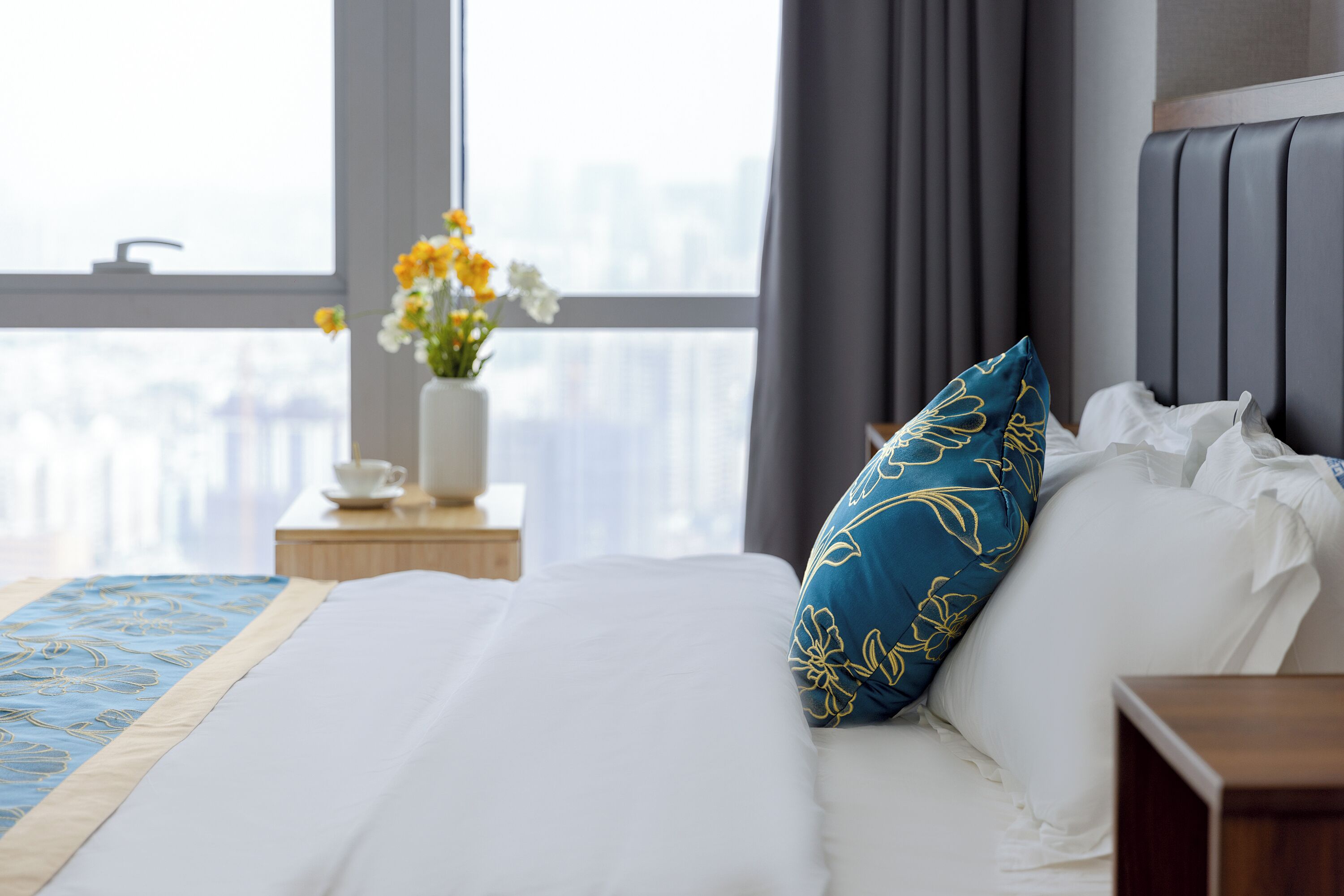Une chambre d’hôtel avec un grand lit, un vase rempli de fleurs et une vue sur la ville par la fenêtre.