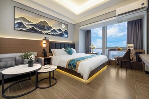 Une chambre d’hôtel moderne dotée d’un grand lit, d’un bureau, d’une table ronde et offrant une vue sur la ville grâce à de grandes fenêtres.