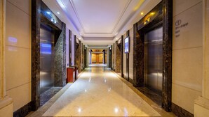 Pasillo de hotel con pisos de mármol, ascensores y una recepción.
