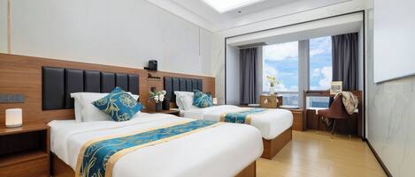 A hotel room with two beds, a desk, a chair, and a large window with a view.
