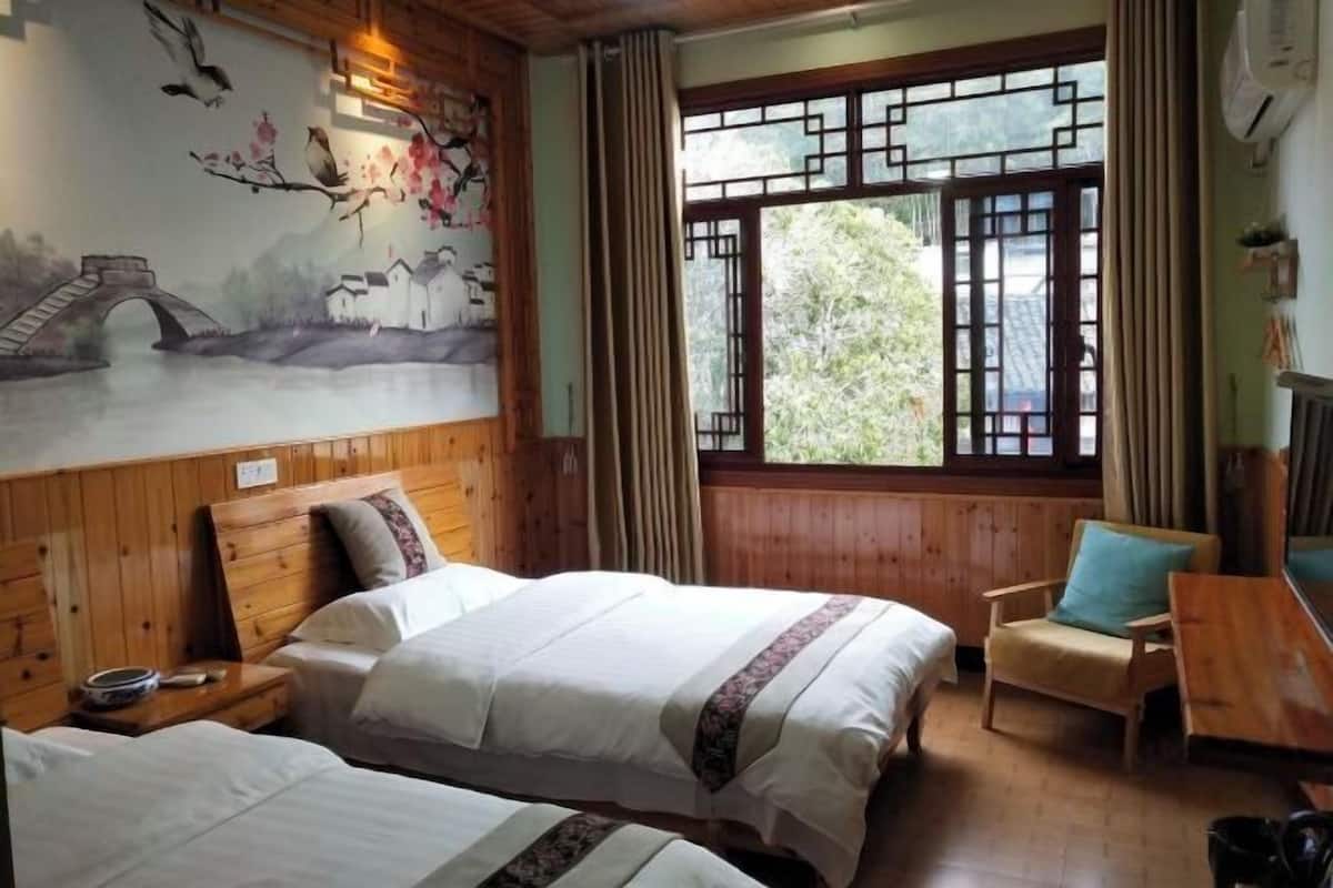 A traditional room with wooden walls, two beds with white linens, a wooden chair, and a mural of a bridge and birds.