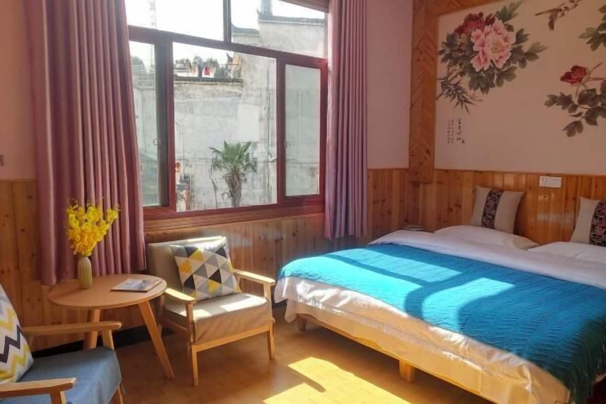 A bedroom with a bed, a chair, a small table, and a window with curtains.