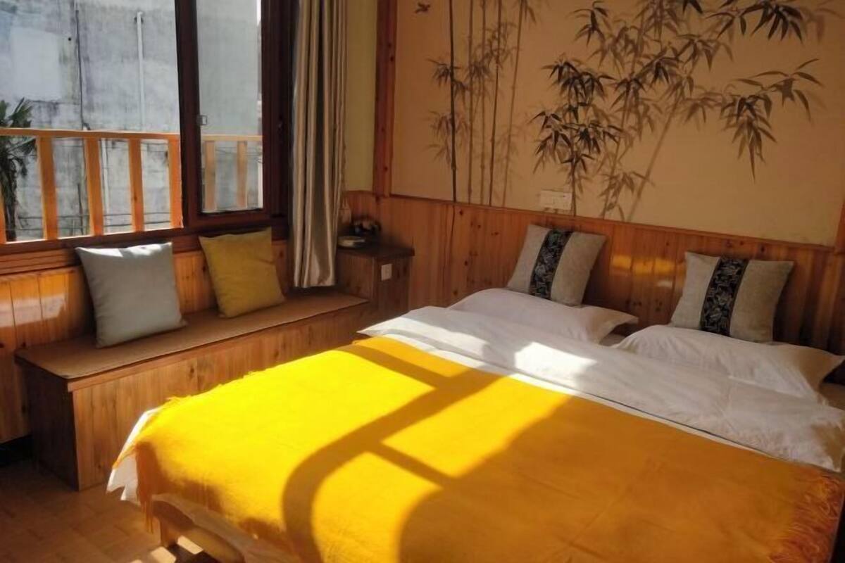A room with a bed, wooden bench, and a large window.