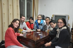 A group of people seated around a wooden table in a room with a window and a television. - Brook Hotel (Wuyuan)