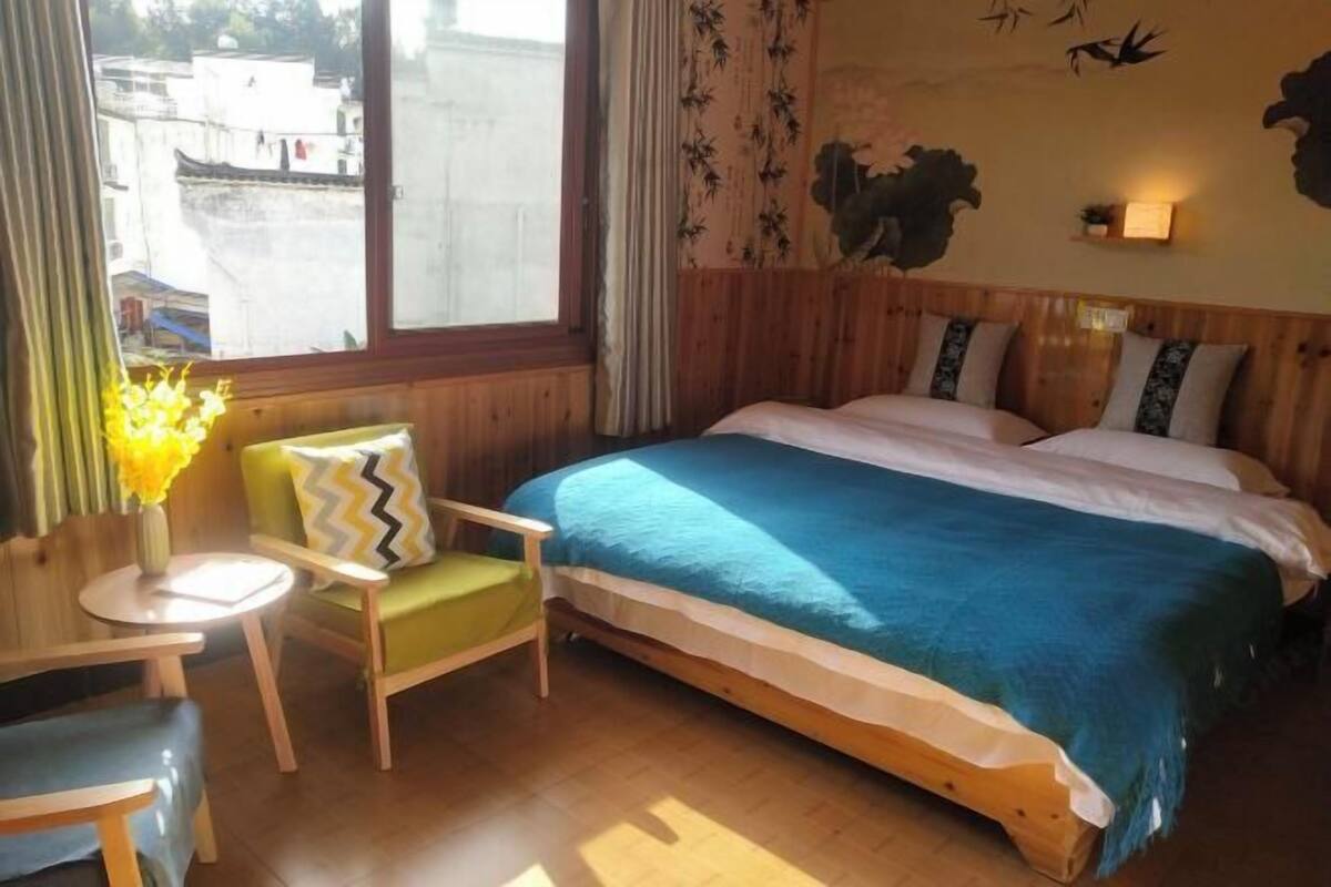 A room with a bed, a chair, a small table, and a window with curtains.