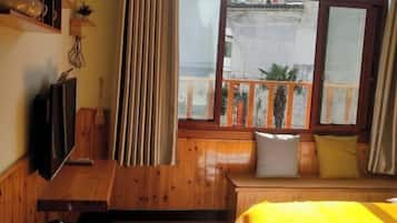 Una habitación con cama, televisor, banco de madera con cojines, ventana con vista y cortina.