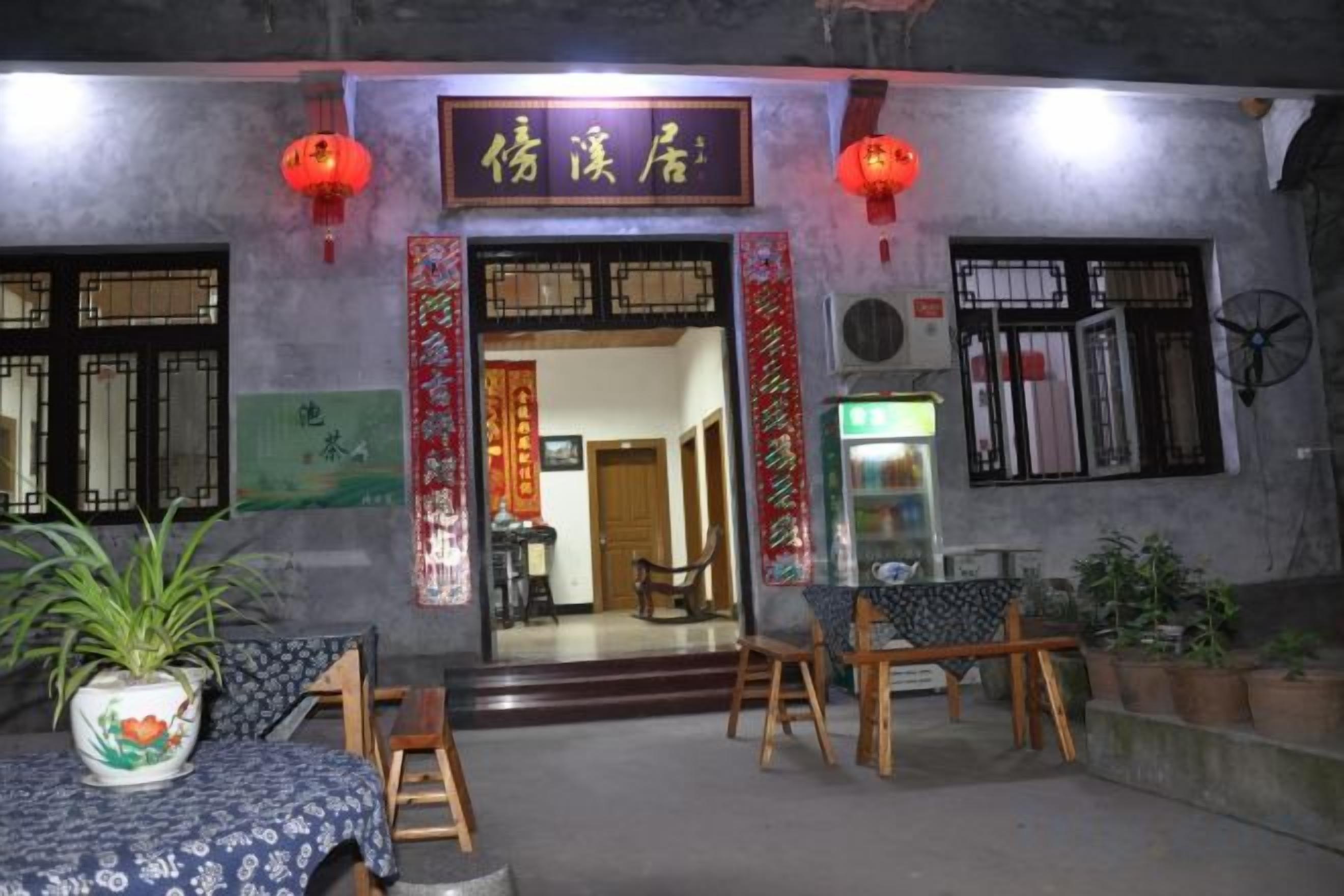 A traditional Chinese restaurant with a signboard, wooden furniture, and potted plants.
