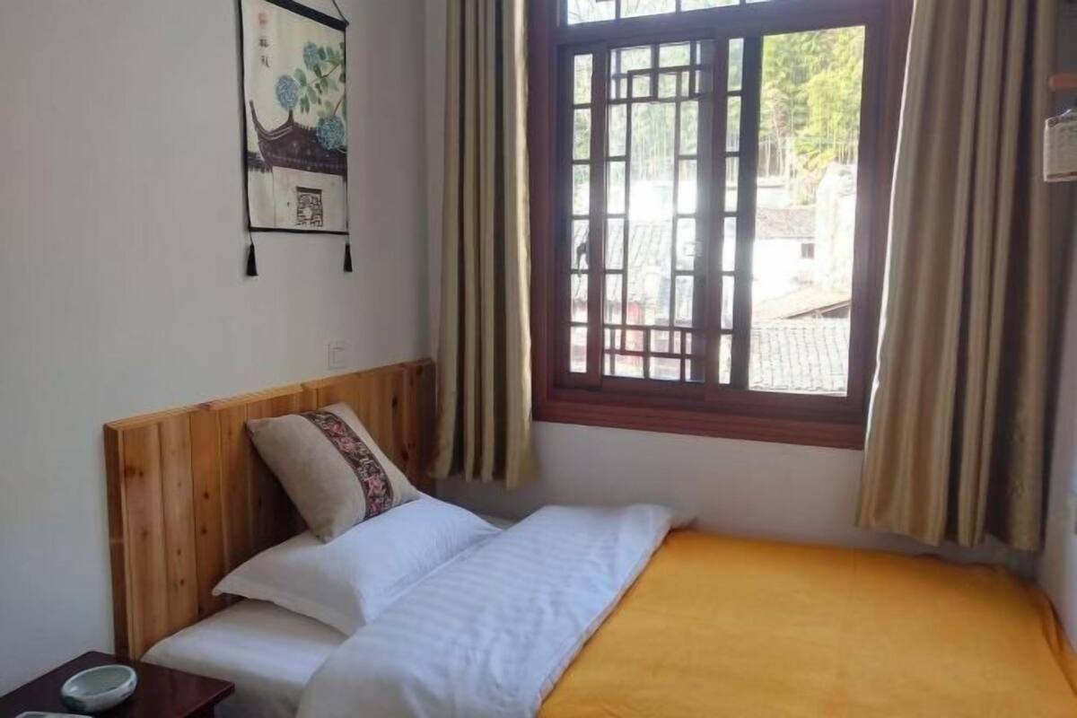 A single bed with a wooden headboard, a window with curtains, and a wall-mounted artwork.