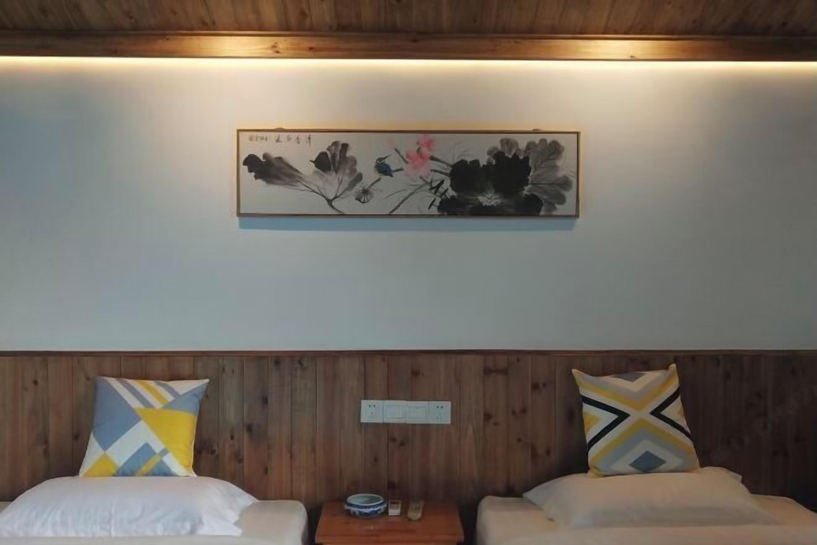 Quarto de hotel com lambris, duas camas com almofadas estampadas, uma mesa pequena com uma tigela e um controle remoto, e uma obra de arte emoldurada na parede.