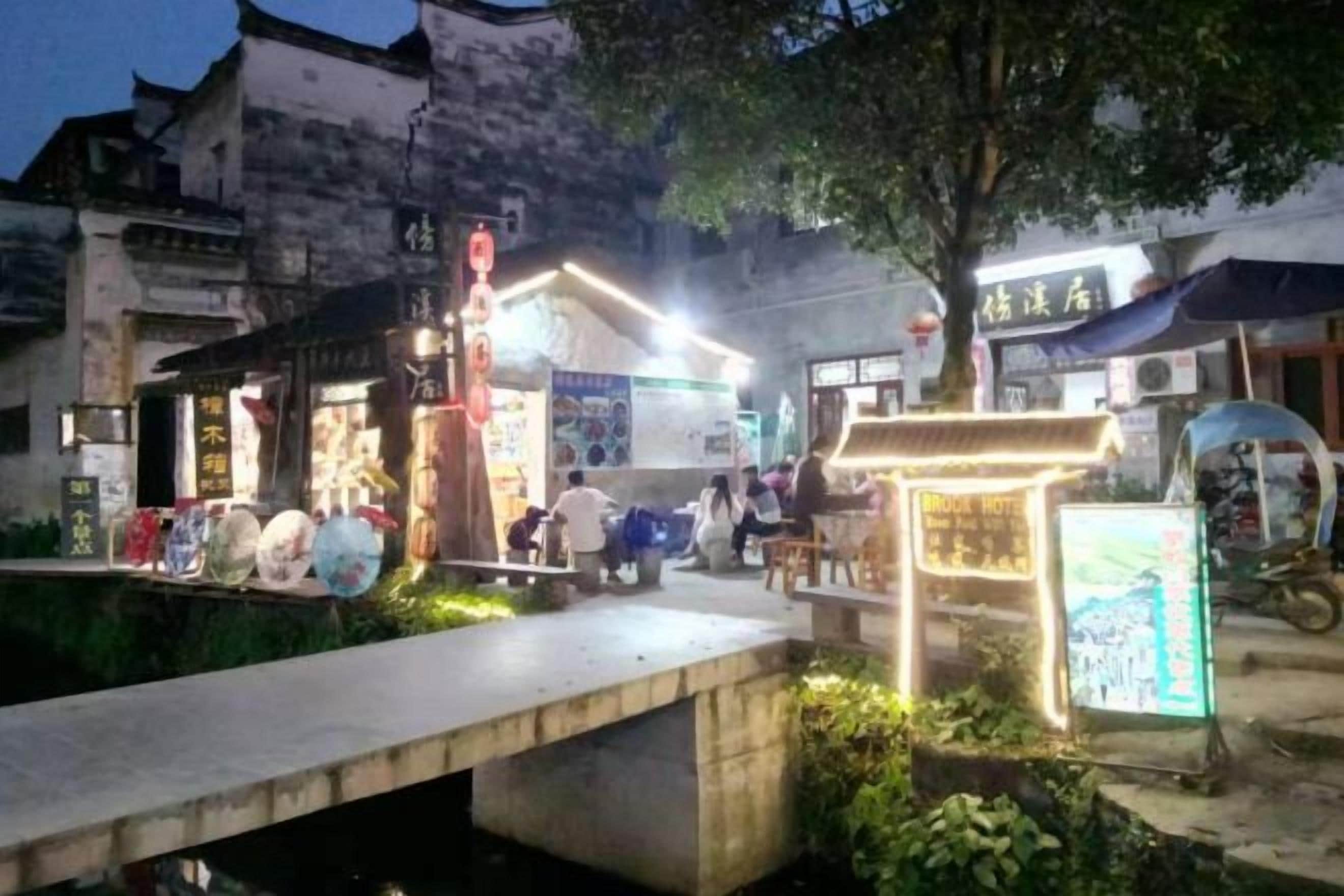 A traditional street scene with a small bridge, shops, and a signboard.