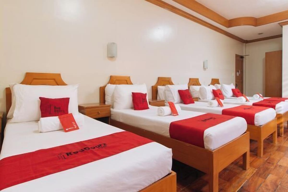 A hotel room with four beds, each with white bedding and red accents.