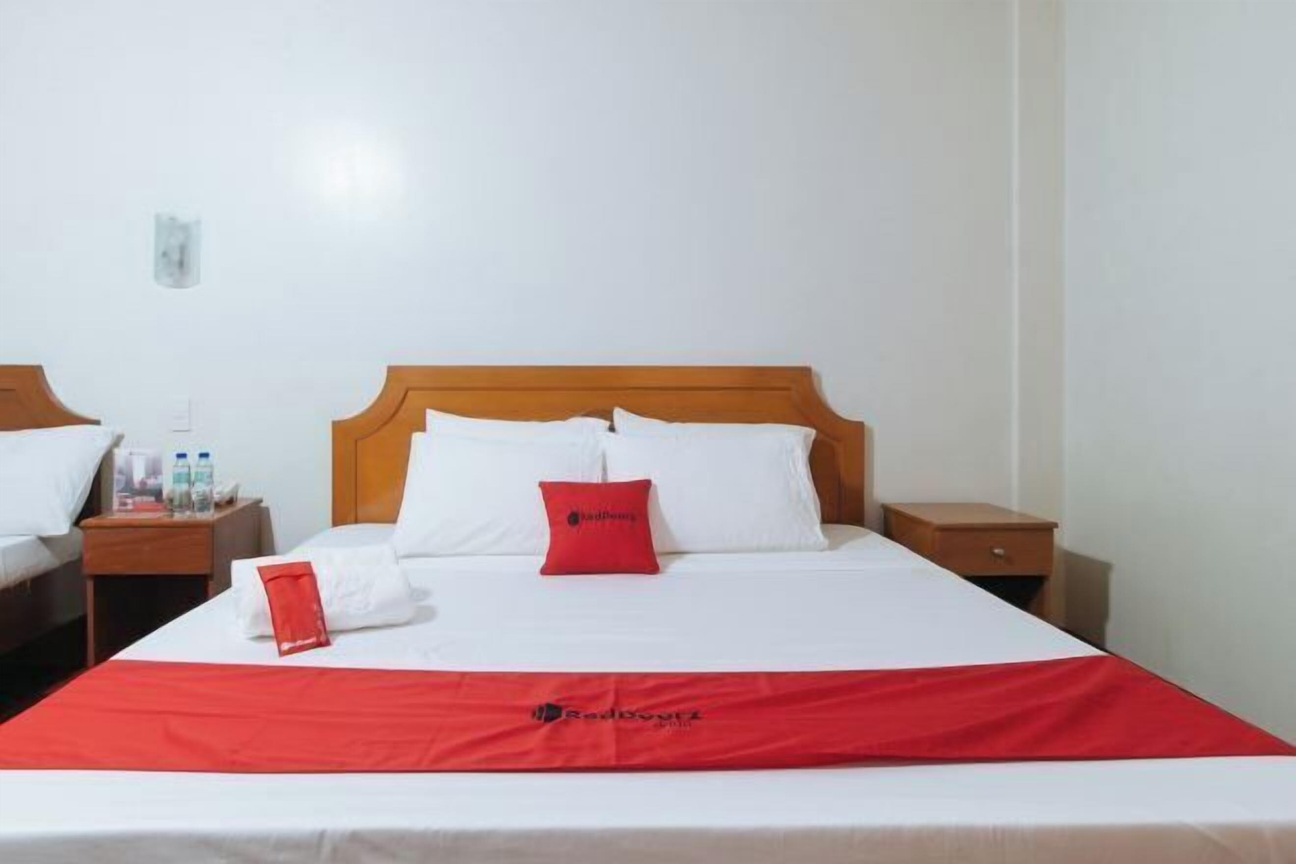 Een hotelkamer met een eenpersoonsbed, twee nachtkastjes en een rode sprei.