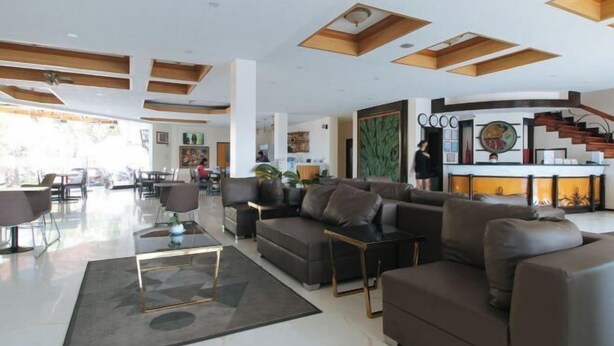 A modern hotel lobby with a seating area, a reception desk, and a staircase. - RedDoorz Premium @ Nick Hotel Gerona Tarlac (Gerona)