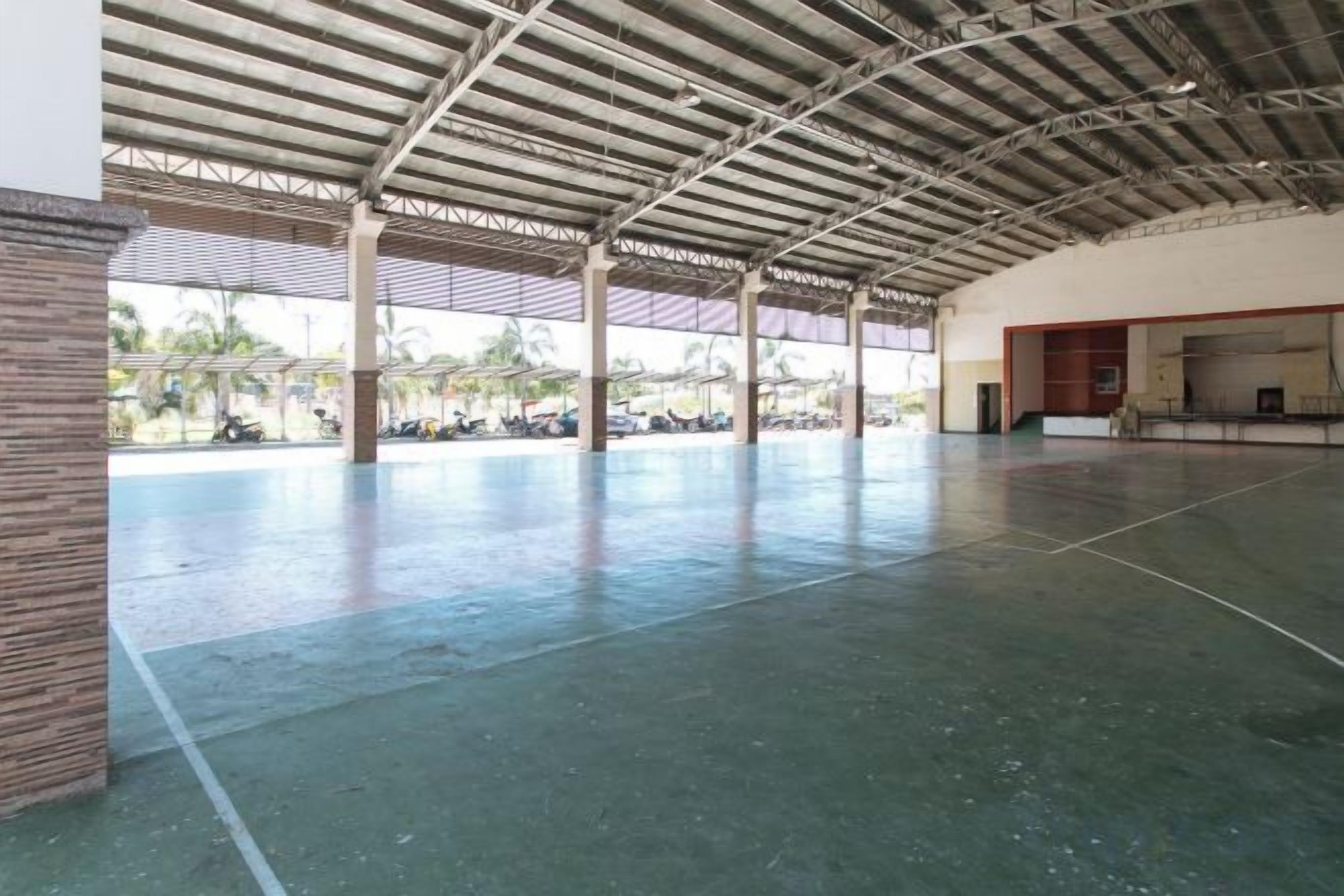 A large indoor space with a high ceiling and a concrete floor, featuring a central open area with a view of the outside.