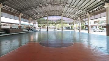 Una cancha deportiva interior con piso rojo y estructura de techo metálico.